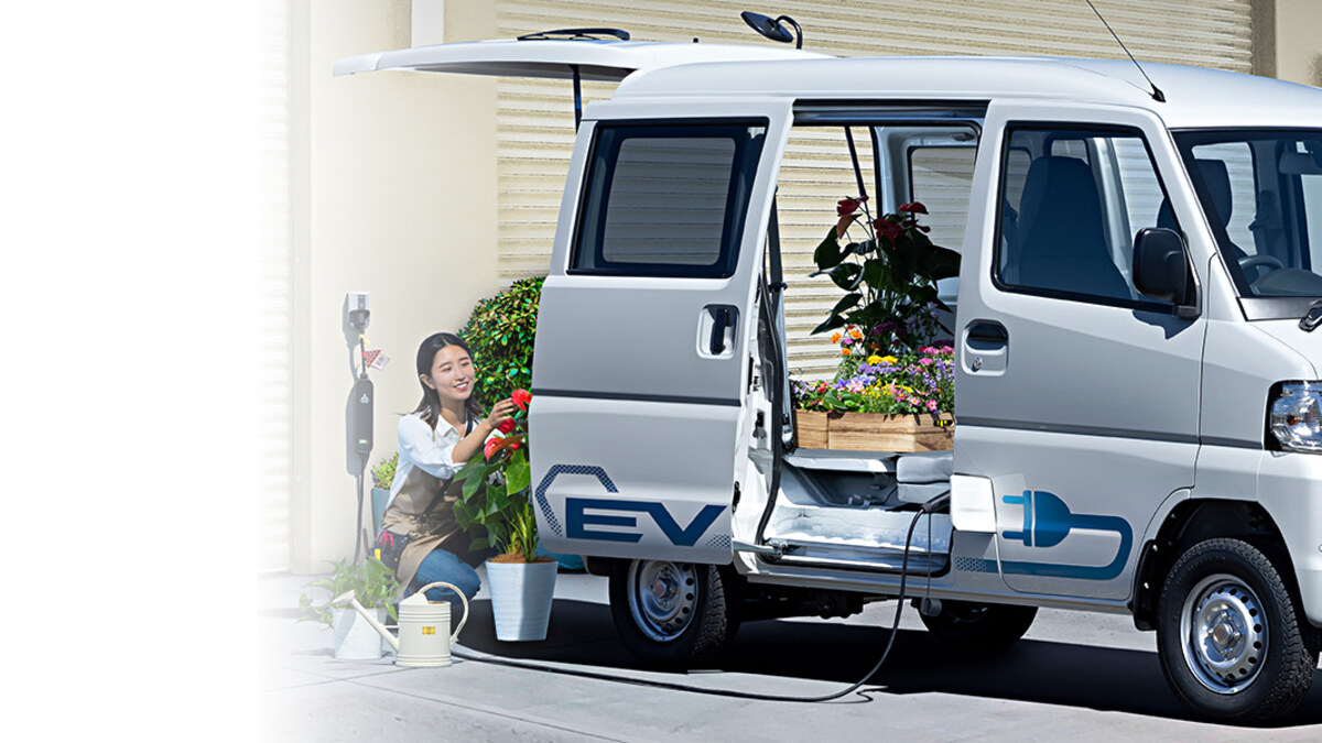 ミニキャブEVの利用シーン。開いたスライドドアと車両脇の充電設備